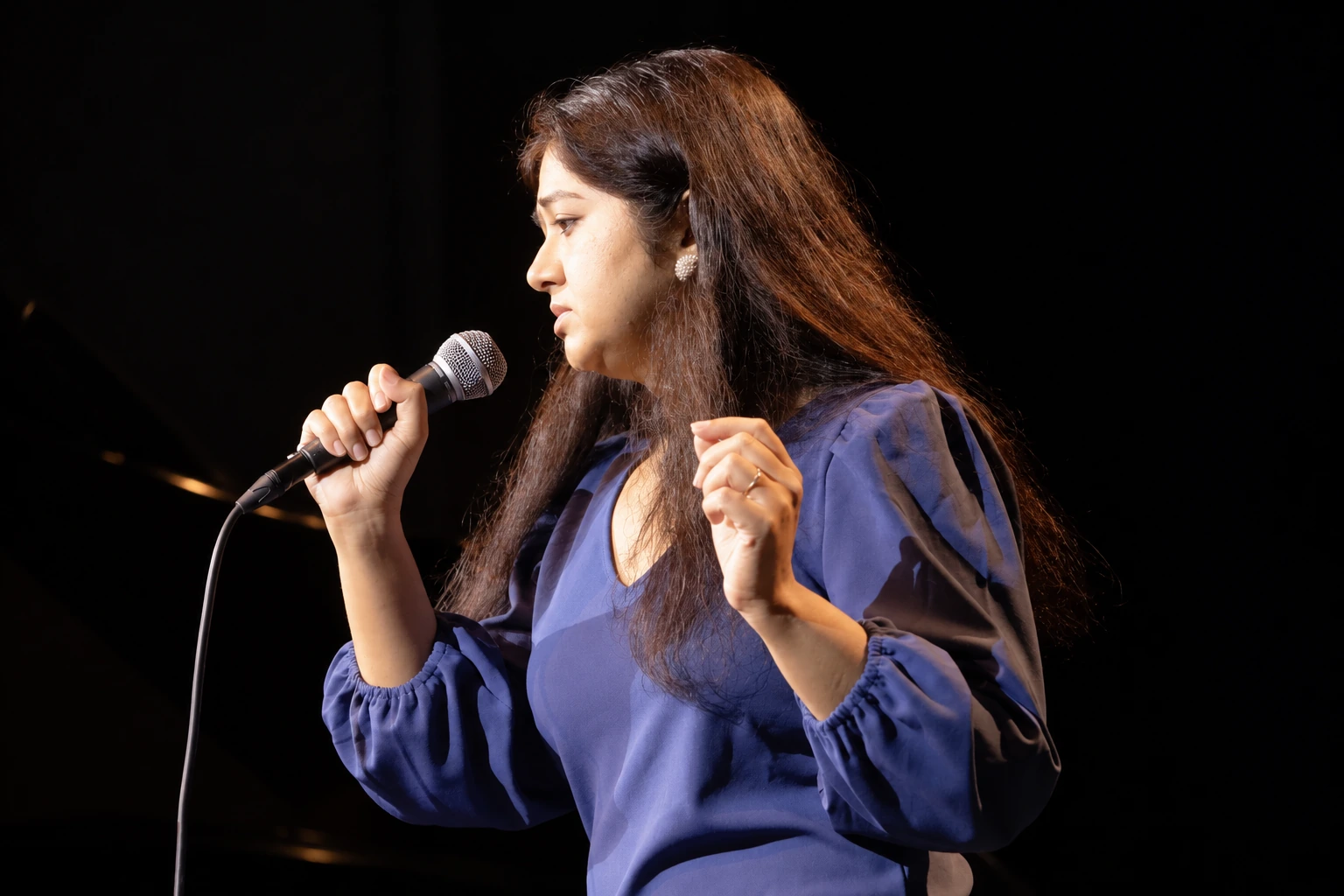 Vocalist in a blue blouse singing into a handheld microphone onstage